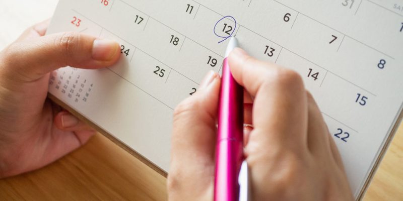 Calendar page with female hand holding pen on desk table