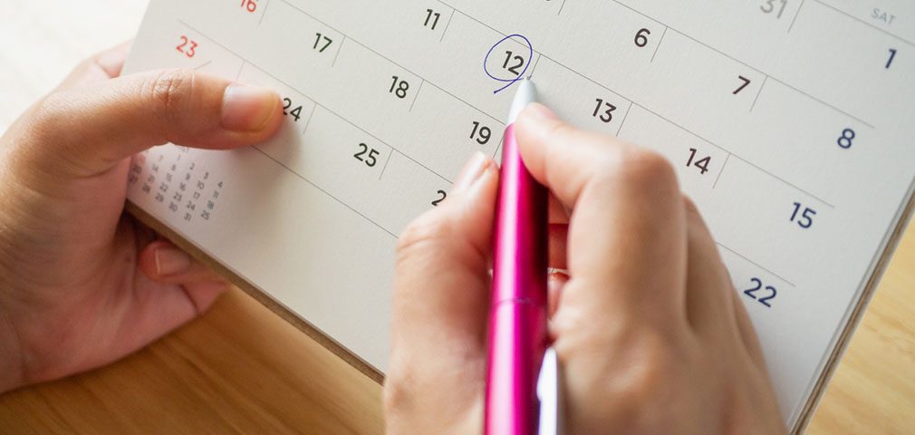 Calendar page with female hand holding pen on desk table