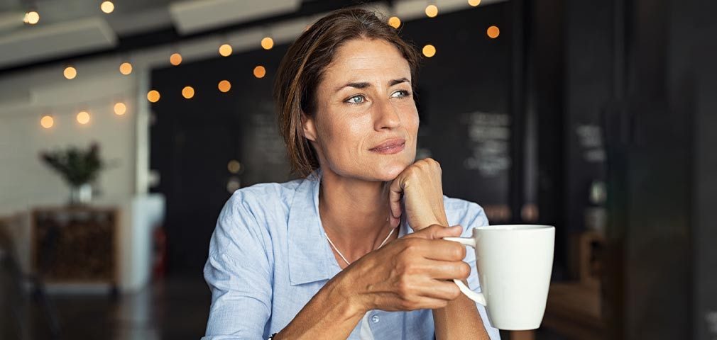 mature woman sitting in cafeteria holding coffee mug while looking away.