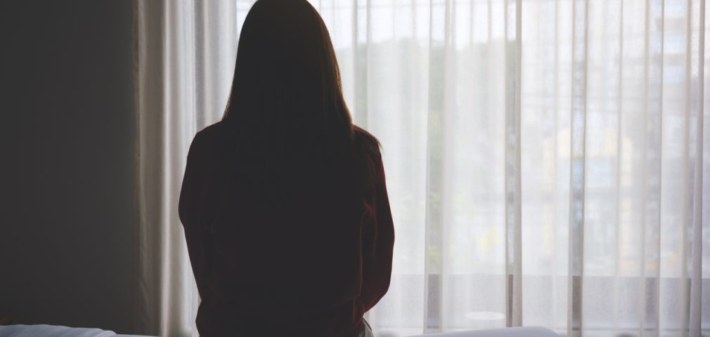 Rear view image of a woman sitting alone on a bed in bedroom