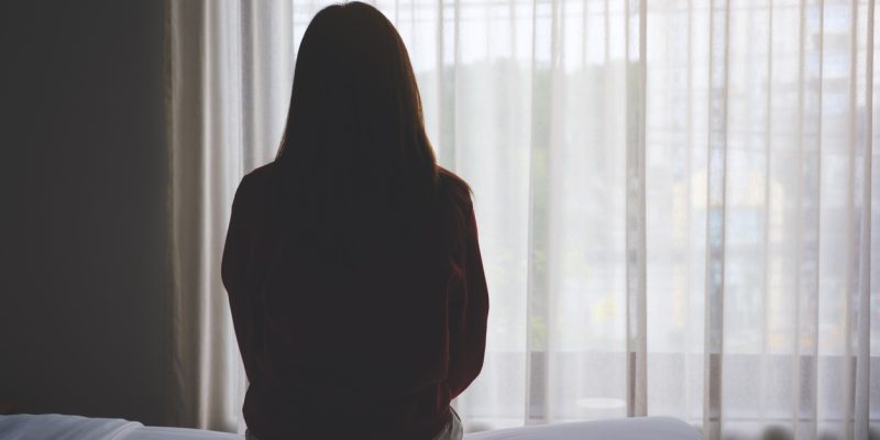 Rear view image of a woman sitting alone on a bed in bedroom